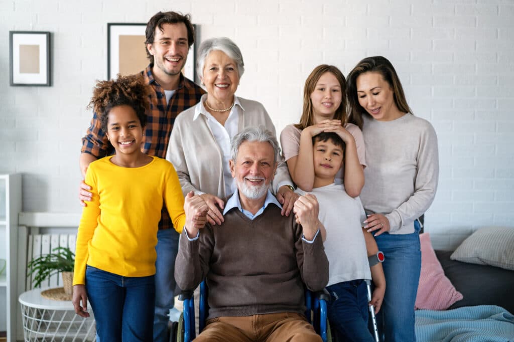 Extended family smiling around grandfather in wheelchair